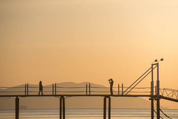 a silhouette of lovers taking pictures on the bridge over the sea of the sunset