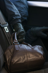 thief's hand steals brown leather bag from car backseat