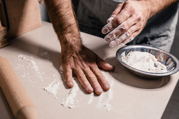 Fototapeta na wymiar Old baker sprinkles flour on table before rolling out dough