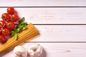 Flat lay view of pasta or spaghetti with bunch of tomatoes, garlic and basil leaves. Old white wooden background or table top