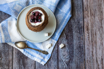 Berry dessert with yogurt in a cup of coconut on a wooden background. Blackberries, raspberries, blueberries, black currants. Blue napkin
