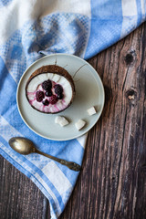Berry dessert with yogurt in a cup of coconut on a wooden background. Blackberries, raspberries, blueberries, black currants. Blue napkin