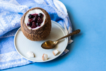 Berry dessert with yogurt in a cup of coconut on a blue background. Blackberries, raspberries, blueberries, black currants. Blue napkin