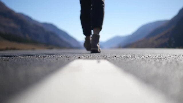 A young woman walks along a big road in sunny weather in the middle of the mountains. Legs close up