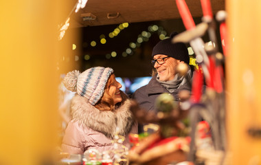 shopping, winter holidays and people concept - happy senior couple at christmas market souvenir shop on town hall square in tallinn, estonia