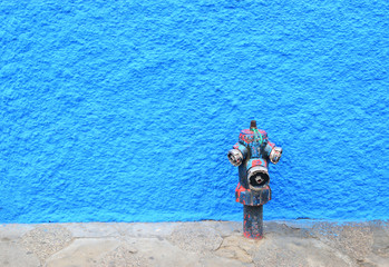  painted Fire hydrant and  blue wall in background An old, weathered fire hydrant with faded paint stands in front of a vibrant blue textured wall, creating a striking urban contrast.