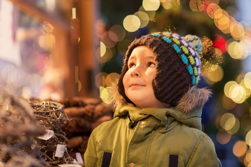 holidays, childhood and people concept - happy little boy at christmas market in winter evening