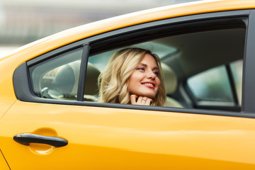 Image of young blonde sitting in back seat of yellow taxi .