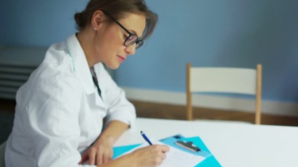 Beautiful female doctor in glasses fills the patient's medical history, and then looking at the camera and smiling. Healthcare and medicine concept, international doctors day