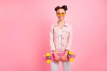 Portrait of lovely lady holding longboard standing with beaming smile wearing jacket isolated over pink background
