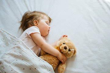 Little baby sleeping on bed embracing soft toy, free space