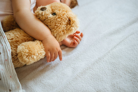 Little baby sleeping and embracing soft toy bear, close-up on hands