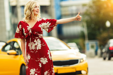 Image of blonde in red dress stopping taxi on summer.