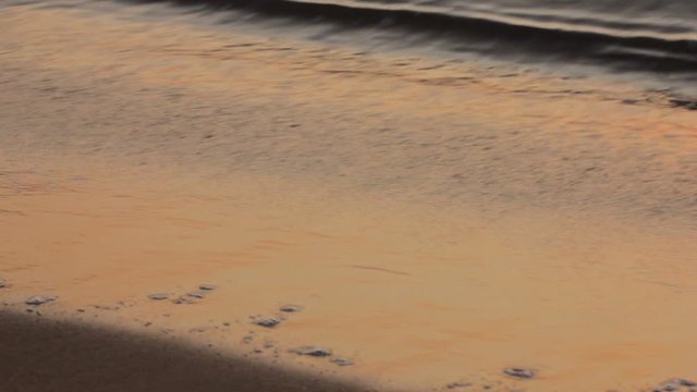 Subdued romantic warm iridescent colors reflecting off the soaking wet sand at sunset and waves overflowing the sand particles.