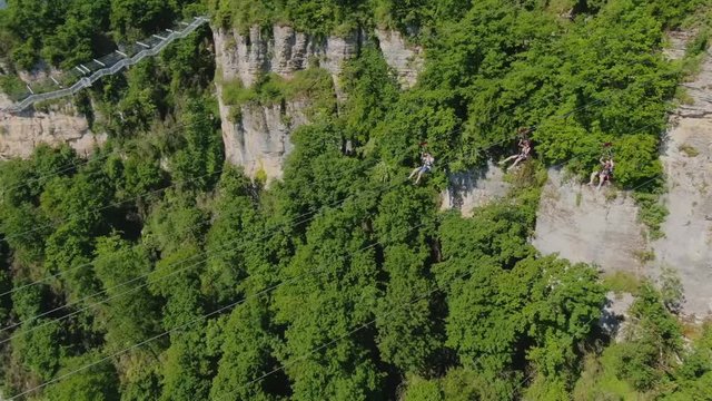 Sochi, Russia - may 2019. Aerial view three people fly over the precipice on cable zip line in Sochi Skypark. Summer sunny day. Green mountain landscape