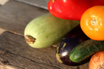 Ripe sweet peppers, zucchini, cucumber, tomato and onions from the infield. Lying on wooden boards, bathed in sunlight.