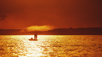 Silhouettes of fishermen in a boat on a sunset background.