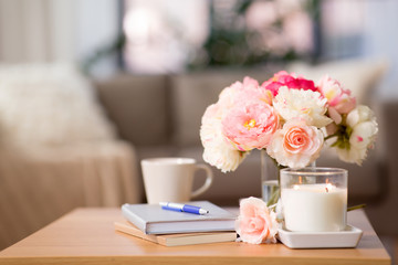 decoration, hygge and cosiness concept - burning fragrance candle, flower bunch, books and pen on wooden table