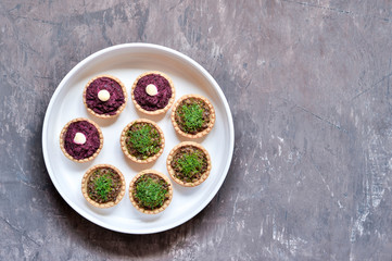 Tartlets stuffed with beetroot and mushroom mince sprinkled with dill in a white plate on a worn vintage background