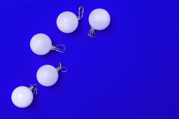 Minimal New Year greeting card with white glass balls on blue colored background. Christmas flat lay border with copy space. Top view.