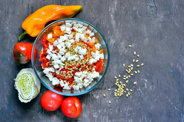 Salad slicing of red and yellow sweet peppers, tomatoes sprinkled with pine nuts and cubes of feta cheese.
