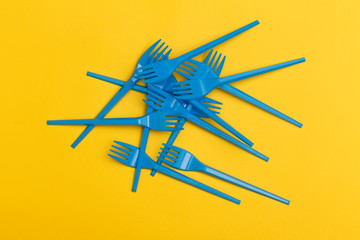 Group of blue disposable plastic forks over a yellow background.