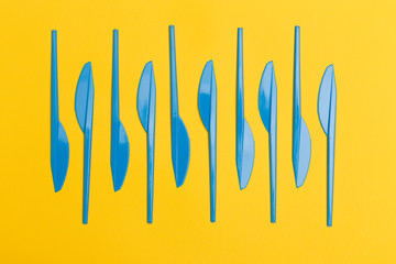 Group of blue disposable plastic knives over a yellow background.