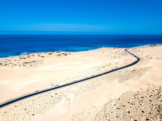 Aerial above view of yellow tropical sandy beach with black long way road and car traveling - ocean blue waves and shore - sunset time with long beautiful shadow - concept of summer vacation