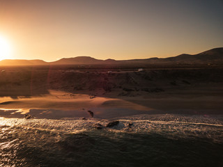 Beach and ocean during sunrise or sunset time with sun behind the mountains in background - beautiful aerial view of nature outdoors - nobody there and travel concept for wild coasts