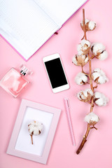 Cotton flowers with smartphone, notepad and perfume bottle on pink background