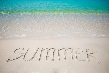 Word Summer handwritten on sandy beach with soft ocean wave on background