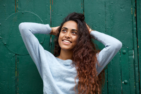 happy Indian girl smiling with hands in hair by green background .