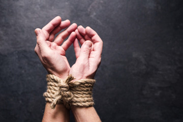 Female hands tied by a rough rope on a dark background, close-up, soft focus. Symbol of bondage, slavery
