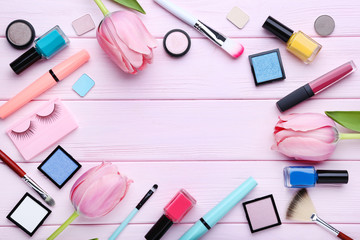 Different makeup cosmetics with tulip flowers on pink wooden table