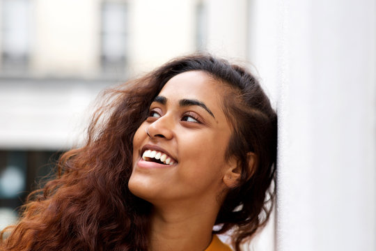 Close up young woman leaning against white wall and smiling