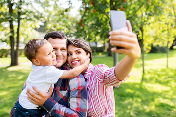 family, leisure and people concept - happy mother, father and little son taking selfie by smartphone at summer park