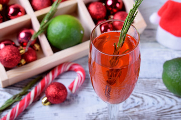 Red alcoholic drink in a tall glass surrounded by Christmas attributes against white wooden background
