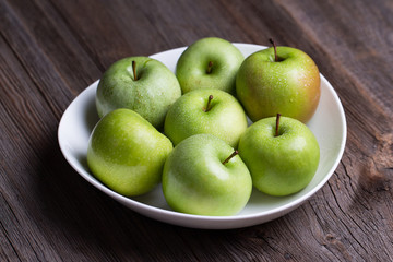Green organic healthy apples in bowl on wooden board. Healthy food