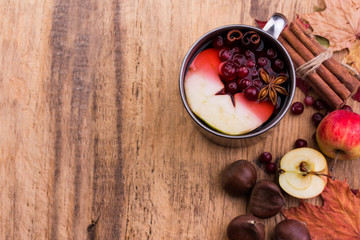 A mug of hot mulled wine, spices, cinnamon, star anise, apple and nuts on a wooden board
