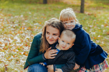 Fototapeta na wymiar Beautiful young mother with daughter and son are walking in the autumn park. close-up portrait