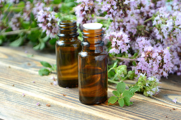Essential oil of oregano in a bottle and fresh flowers on a wooden table Natural cosmetics and aromatherapy