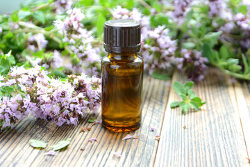 Essential oil of oregano in a bottle and fresh flowers on a wooden table Natural cosmetics and aromatherapy