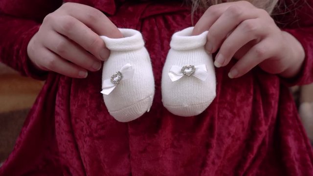 A young pregnant woman applies booties to her stomach. Woman in a red dress plays with booties