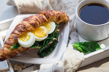 Coffee and croissant with egg and sauteed spinach for breakfast