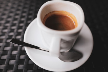 Details with a white ceramic cup of coffee and a stainless steel spoon on a table in a coffee shop