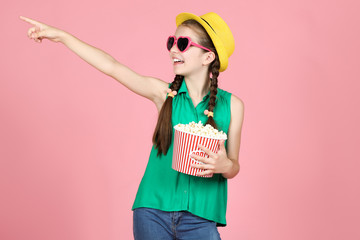 Beautiful young girl holding bucket with popcorn on pink background