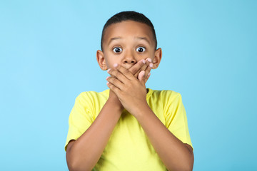 Cute american boy closing mouth by hands on blue background