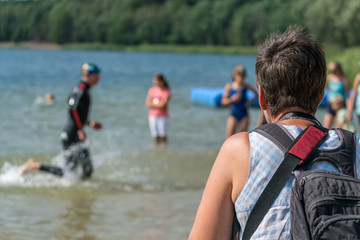 Woman watching a triathlete running out of the water to the transition zone at a triathlon...