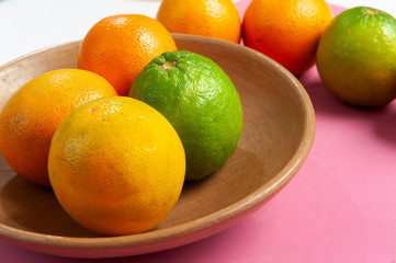 Fruit orange, yellow, green.Dish color clay, brown.Pink background.Close up.