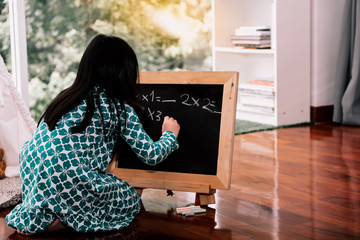 Fototapeta na wymiar A 6 year old girl is practicing math broblems On a small blackboard At her house on vacation, concept to child and education